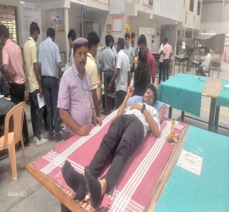 A donor lying on a camp bed giving blood while others stand around the camp