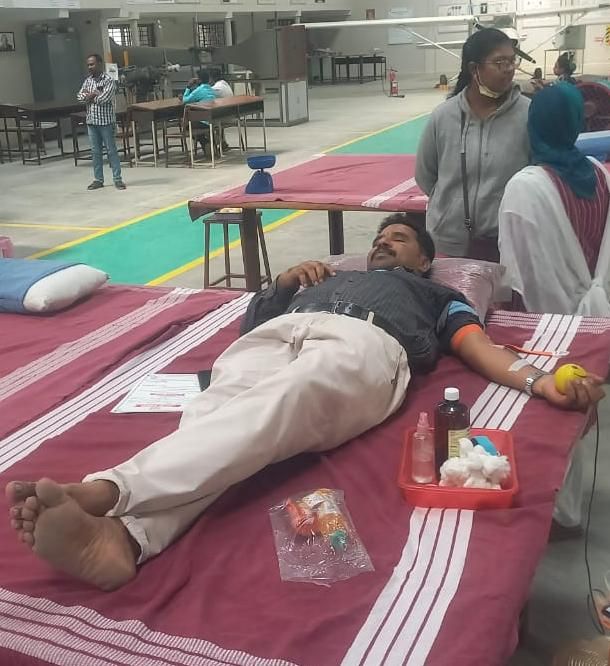 A donor lying on a camp bed giving blood as volunteers look on