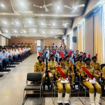 Cadets in khaki uniform, red sashes and white gloves seated in a row, their berets topped with red plumes