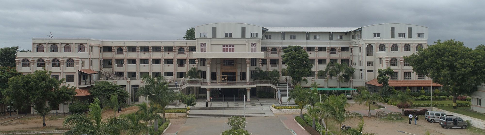The front of a PMC Tech campus building, its entrance portico set among trees under a cloudy sky