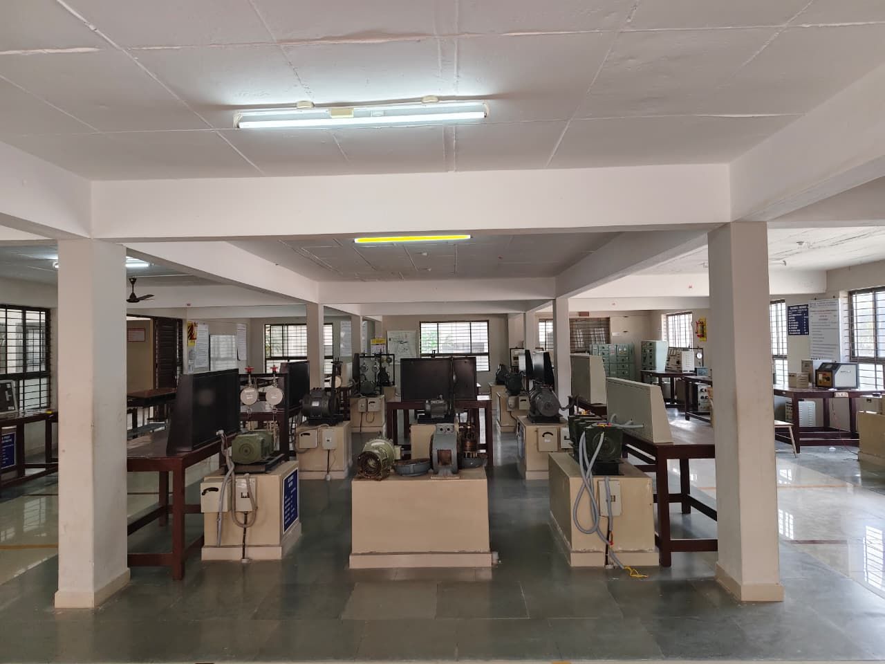 A tall hall of square pillars seen from one end, with machine sets and control panels on plinths and benches down the middle of the floor.