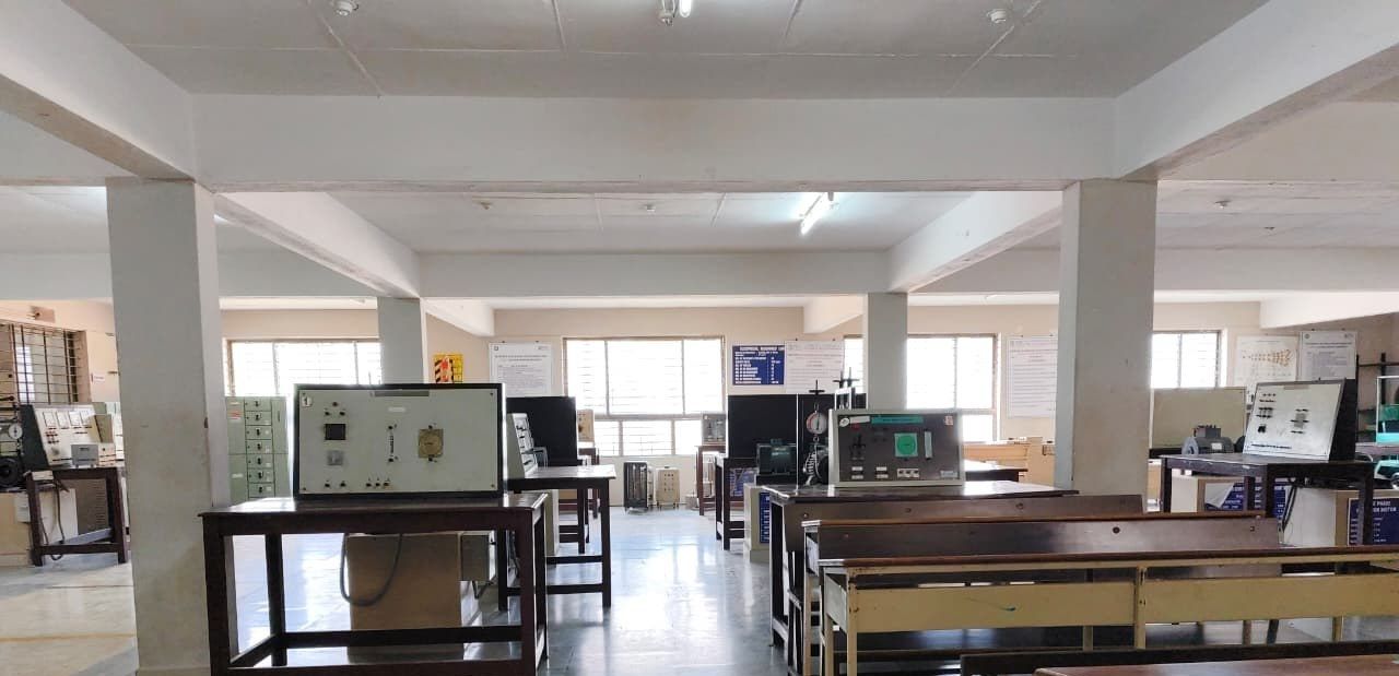Test benches with control panels in the foreground of a hall with pillars, and long wooden benches along the right.