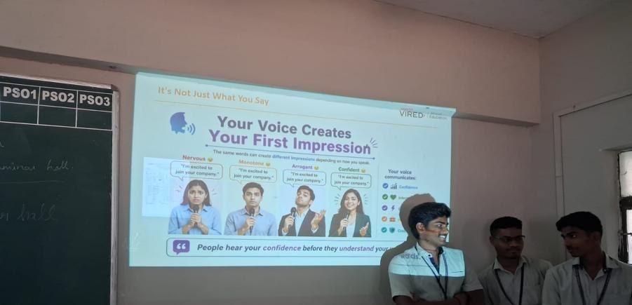 Three students stand at the front of a classroom beside a projected slide titled “Your Voice Creates Your First Impression”.