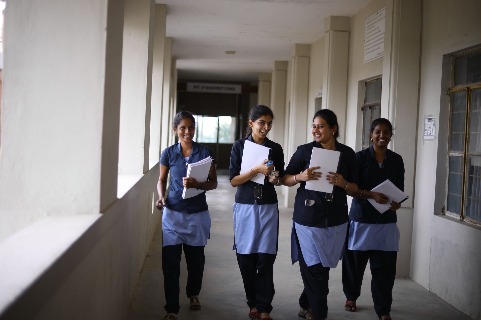 Four PMC Tech students walking along a corridor, carrying papers and smiling