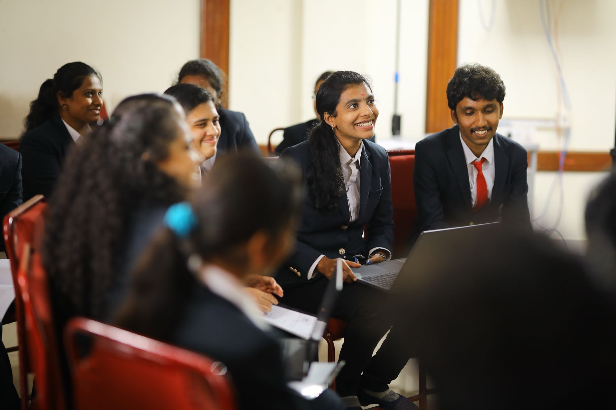 PMC Tech students in dark blazers smiling together in a group session, one with a laptop