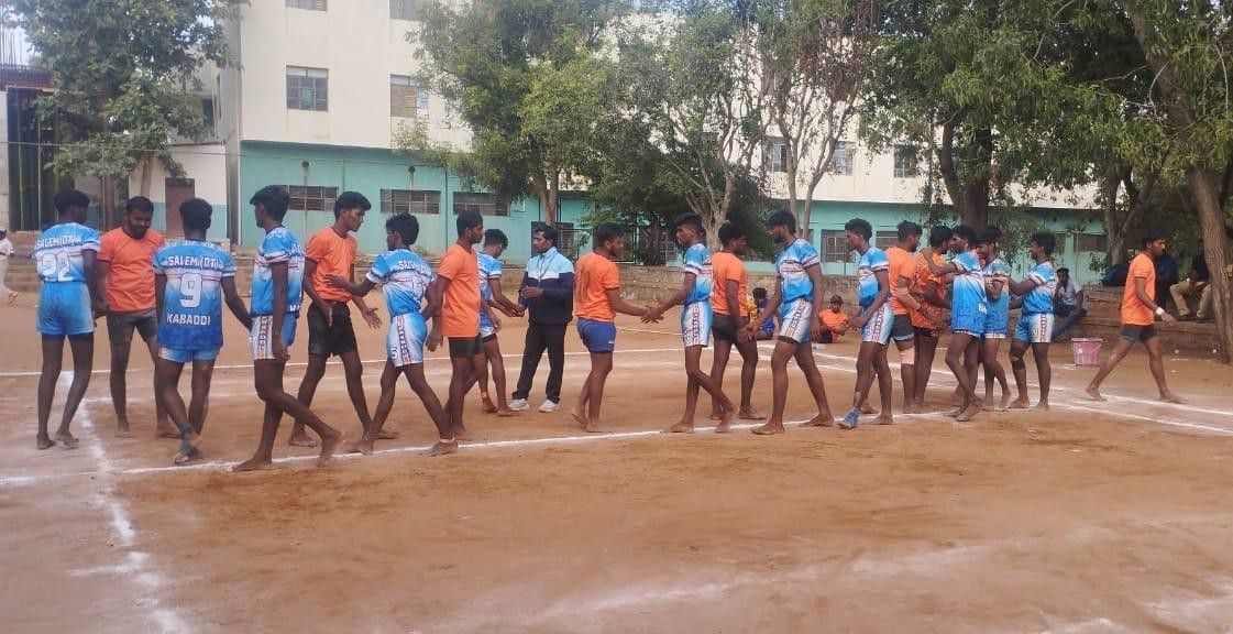 Two kabaddi teams, in blue and in orange, lined up facing each other on an earth court