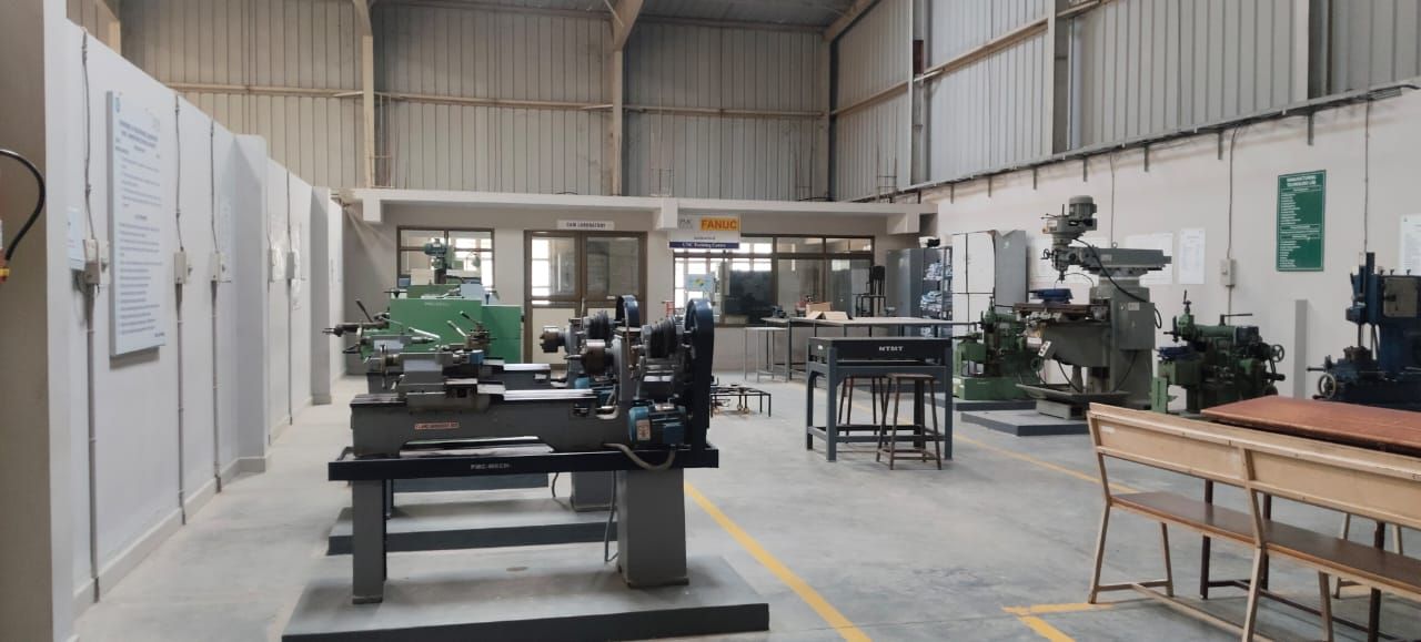 A workshop hall with lathes in the foreground and other machine tools on the right, and a glazed room at the back marked with a FANUC sign.