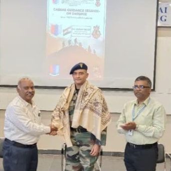 An officer in uniform, a shawl over the shoulders, shaking hands with a man in a white shirt while another man looks on