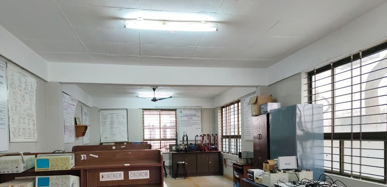 A bright hall with wooden benches carrying oscilloscopes and instruments, barred windows on the right and a grey cabinet at the back.